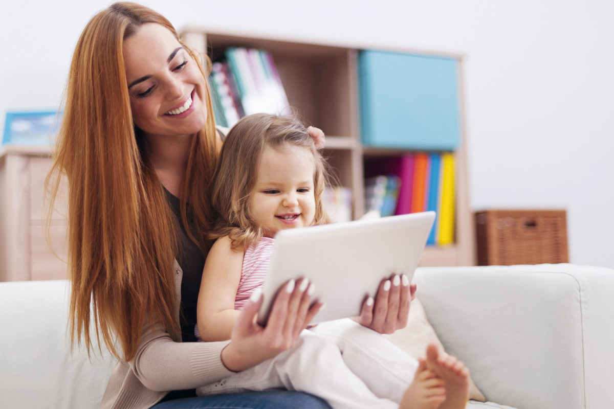 Mutter und Tochter schauen auf ein Tablet und begeben sich auf Kita-Suche in Berlin.