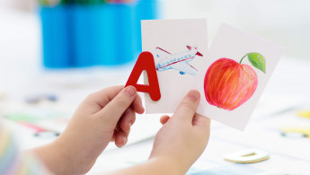 Kind hält Buchstaben mit dazugehörigen Objekten in der Hand