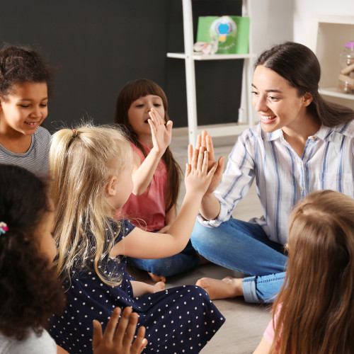 Freundliche Erzieherin in Kita-Gruppe gibt einem Kind ein High Five – positive Interaktion