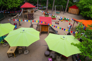 Vogelperspektive der Außenanlage der Kita Frohnatur, Spielplatz mit vielen Sonnenschirmen und Girlanden