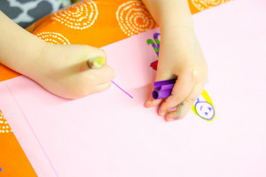 Kinderhände halten Buntstifte und malen Menschen auf Papier