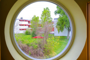 Rundes Fenster mit Ausblick auf den grünen Innenhof der Kita Senftenberger Ring
