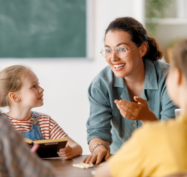Erzieherin erzählt Kindern begeistert etwas – sie hören lächelnd zu