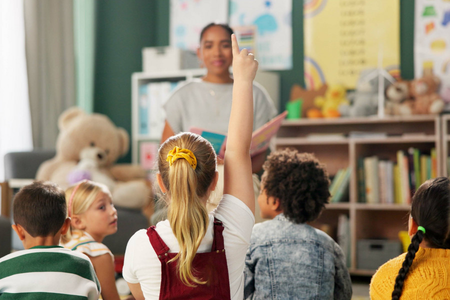 Gruppe Kinder sitzt vor Erzieherin – ein Kind meldet sich